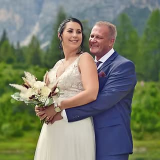Fröhliches Brautpaar mit Strauß bei Hochzeit in den Bergen